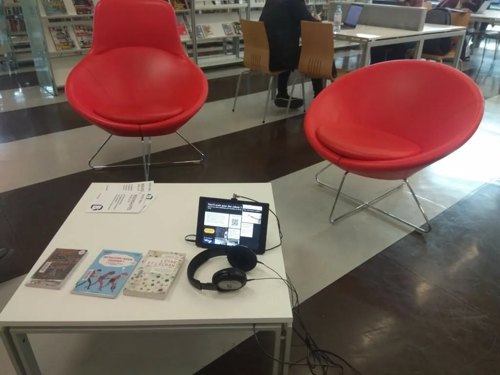 Une tablette posée sur une table basse de la bibliothèque, entre des livres et un casque audio.